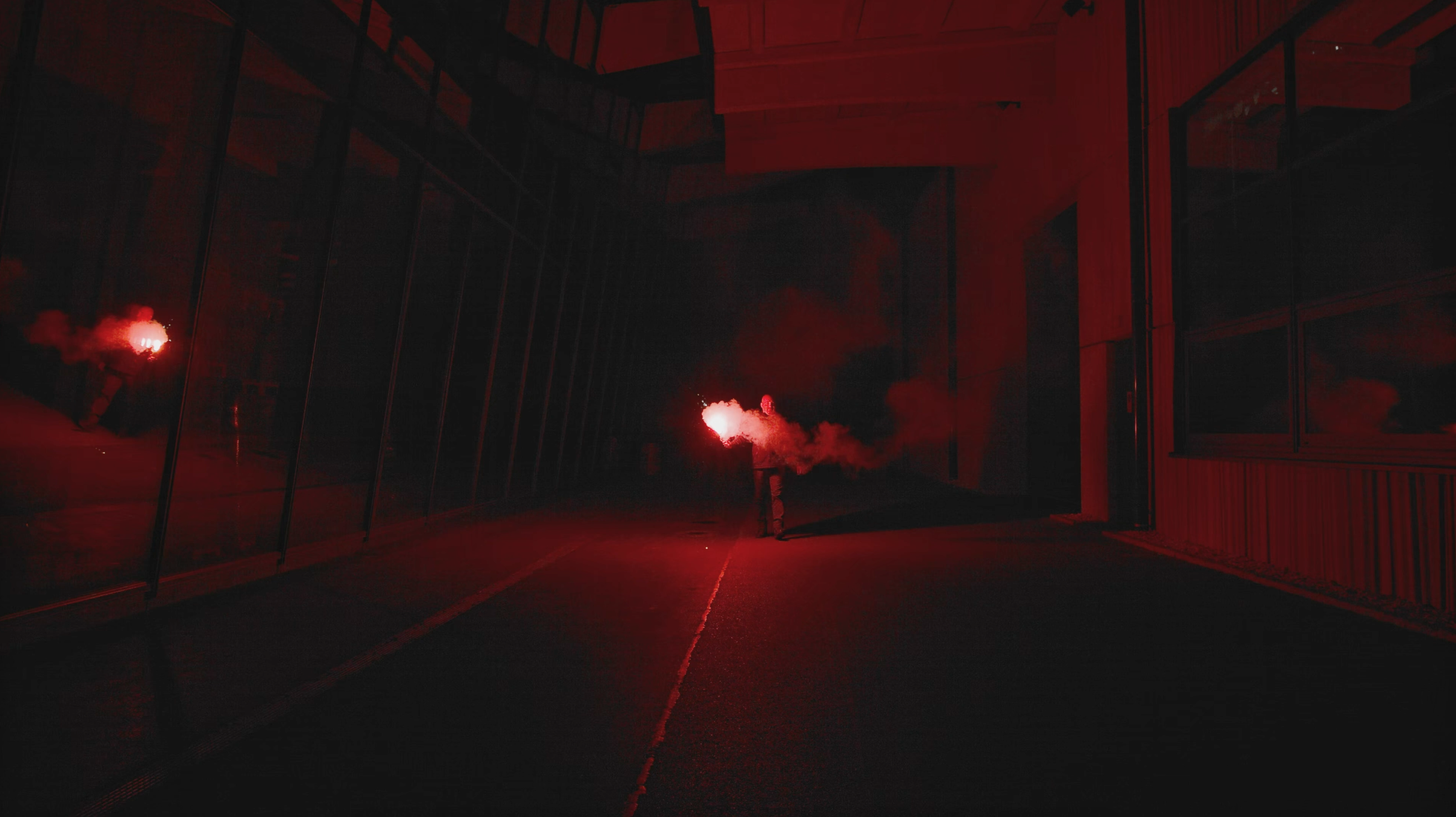 Eine Person hält eine rote Fackel in einem dunklen, industriell anmutenden Raum mit dramatischer Beleuchtung.